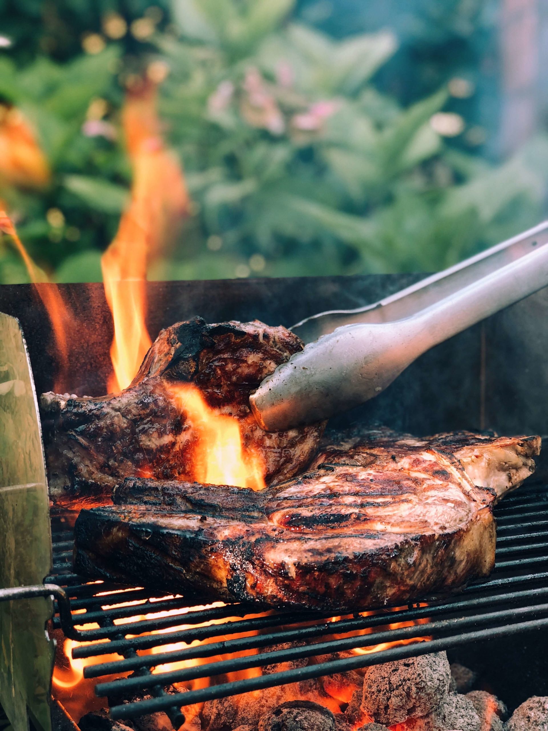 Steaks on a grill being turned with tongs and flames around one steak