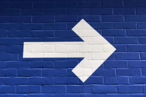 white arrow pointing to the right on blue brick background