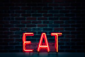 Red neon sign saying EAT on black brick background